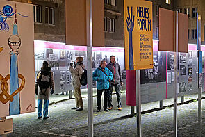 Auf dem Bild sieht man Menschen, die sich die Plakatausstellung "Haltet die Freiheit hoch" anschauen, die anlässlich des Jubiläums zu 35 Jahre Mauerfall.