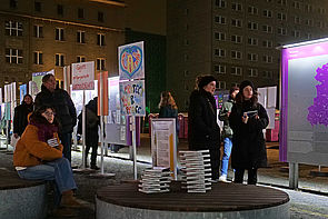Auf dem Bild sieht man mehrere Menschen, die sich die Open-Air-Ausstellung auf dem Campus der Demokratie bei Nacht anschauen. Dazu stehen Plakate, die anlässlich des Jubiläums zu 35 Jahre Mauerfall zum Motto "Haltet die Freiheit hoch" erstellt wurden.