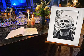 Auf dem Bild sieht man ein Kondolenzbuch auf einem Bartresen liegen. Dahinter stehen zwei Kerzen. Rechts daneben befindet sich eine Staffelei mit einem Schwarz-Weiß-Foto von Olaf Weißbach.