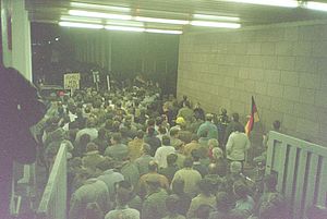 Auf dem Bild sieht man eine große Menschengruppe, die sich dicht gedrängt durch ein geöffnetes Tor mit einem Tunnel zwängt.