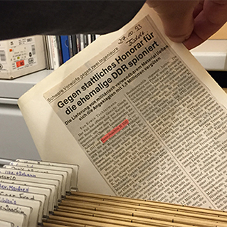Hand zieht archivierten Zeitungsartikel aus Aktenschrank
